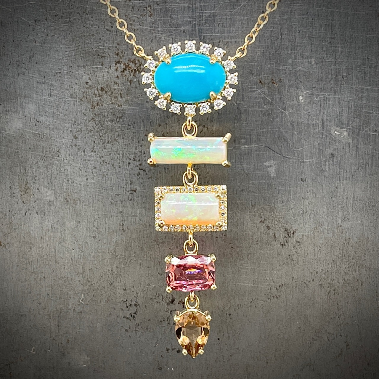 Front view of 14k yellow gold pendant presents a tapered sequence of colored gemstones, highlighted by diamond accents