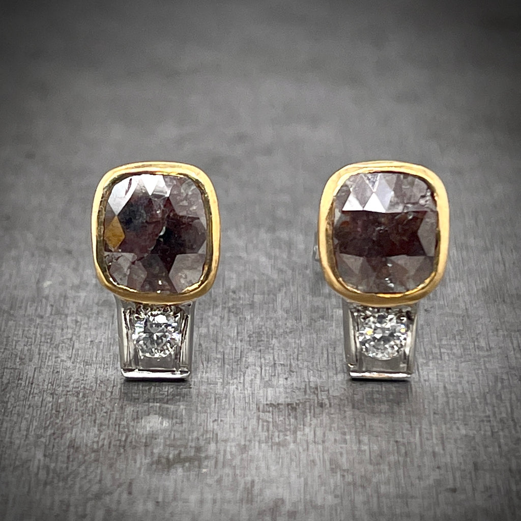 Full view of red diamond studs. A rectangular quilted cut red diamond is the focal point, set in 18 karat yellow gold. Set below the red diamond is a round brilliant diamond set in a rectangular platinum mounting.