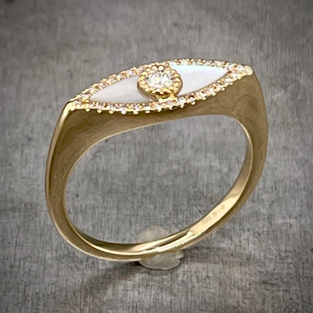 Full angled view of mother of pearl evil eye ring standing up on gray background.