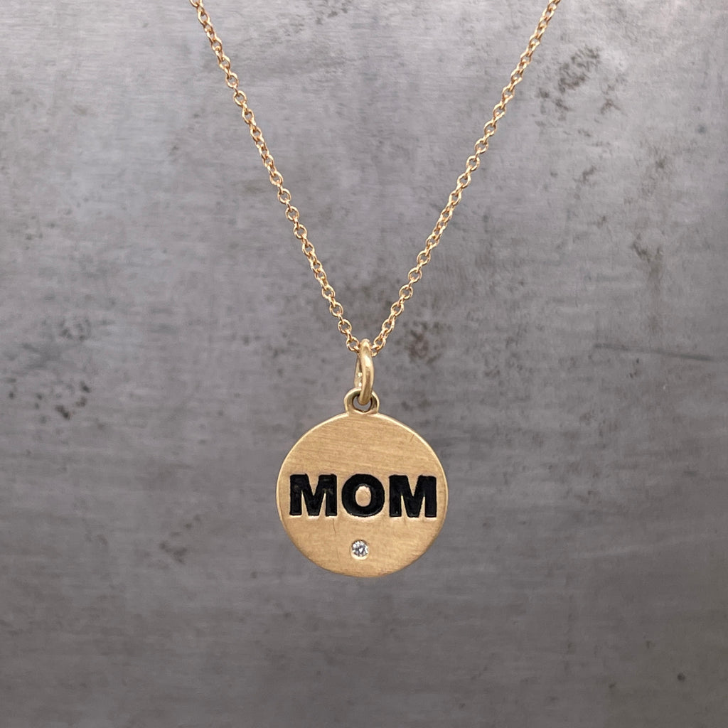 Front view of 14K yellow gold pendant engraved with "MOM," featuring one flush set diamond.