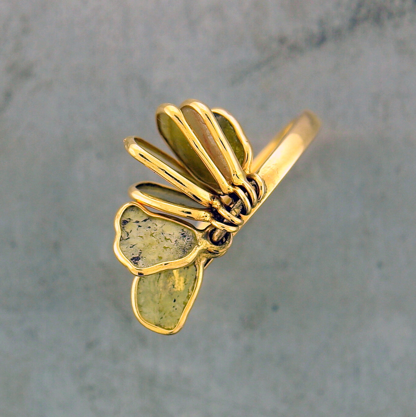An aerial view of the top of the 14 karat yellow gold diamond slice ring. You can see the right shoulder of the ring, the left shoulder is covered by two diamond slices that lay flat. Here you can better see the inclusions of the diamond. The remaining four diamond slices are hanging from their bail where you mainly see the edge of the bezel setting.