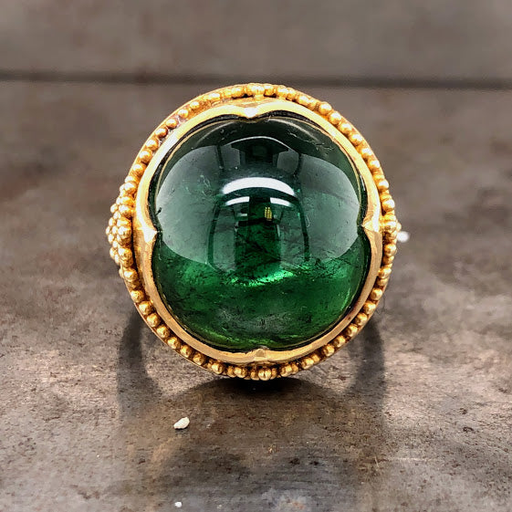 Frontal view of green tourmaline ring. Here you can see dark green inclusions within the tourmaline. The tourmaline is encompassed in yellow gold with three claw like prongs extending from the Northern, Eastern, Southern and Western edges.