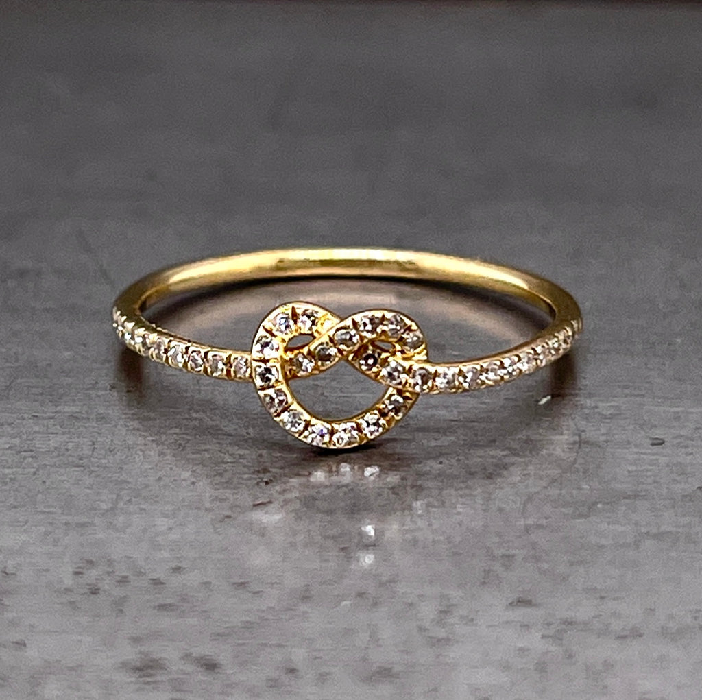 Frontal view of Love Me Knot Ring laying down. A yellow gold ring that features what looks like a pretzel knot in the center of the ring. The face of the ring is set with a layer of round brilliant diamonds.