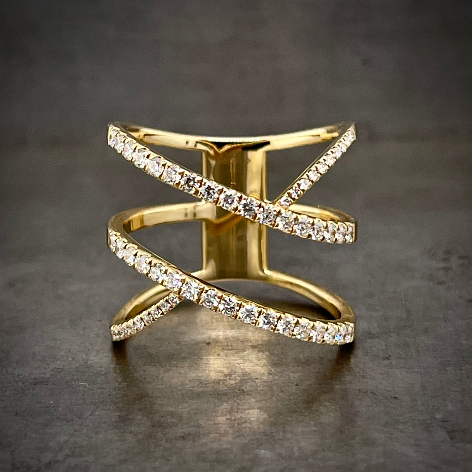 Frontal view of three in one diamond ring. Two bands run diagonally, parallel to one another. A third band starts to run through them perpendicularly but does not follow through the middle of the two parallel bands. All three bands feature a row of round diamonds set onto their surface and they all join together in the back of the ring.