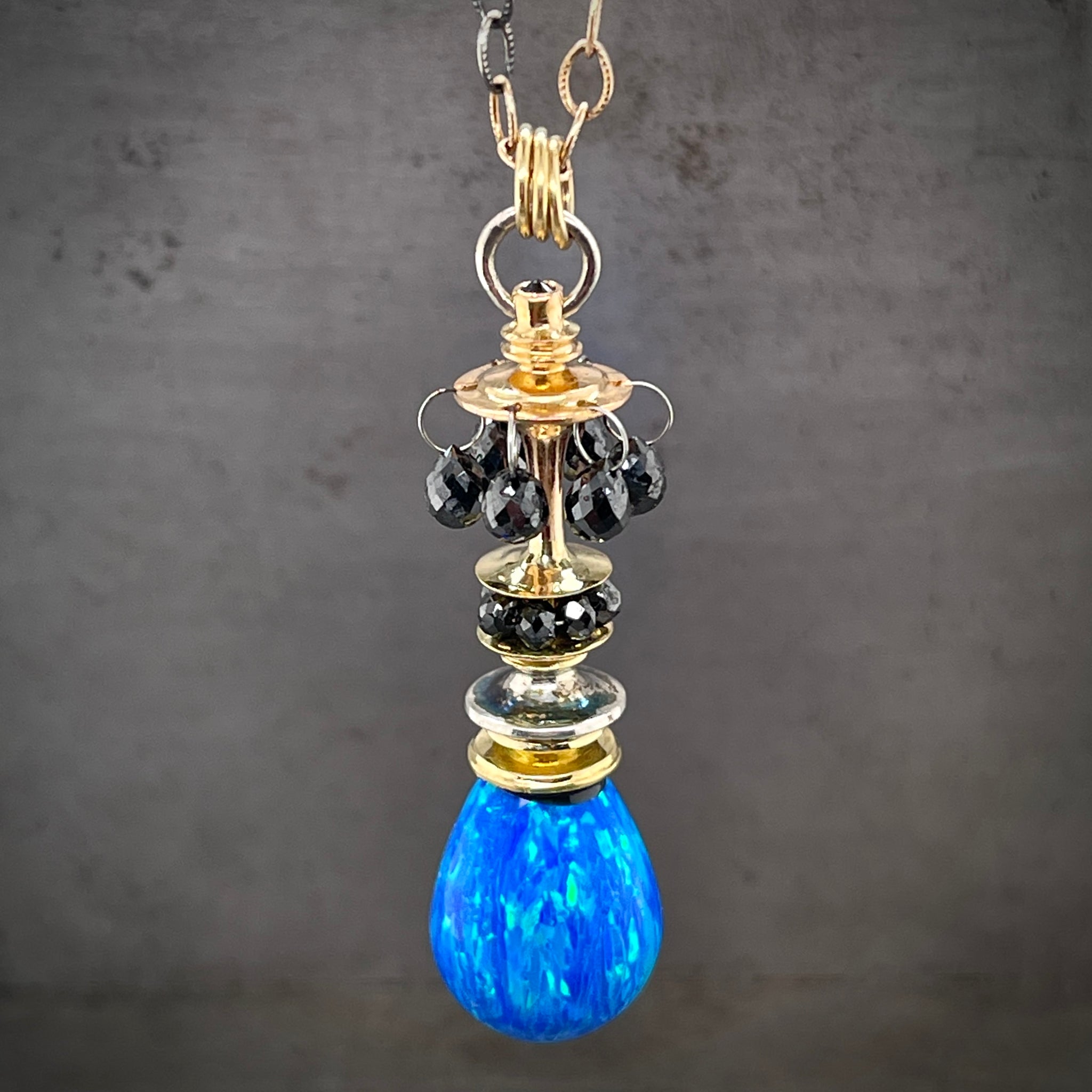Close up view of opal and black diamond parasol pendant. This parasol features one opal strung on 18 karat white, yellow and rose gold. Black Diamond are strung around the parasol and black diamond briolettes hang off of the pendant. Bezel set on the top is a single black diamond.