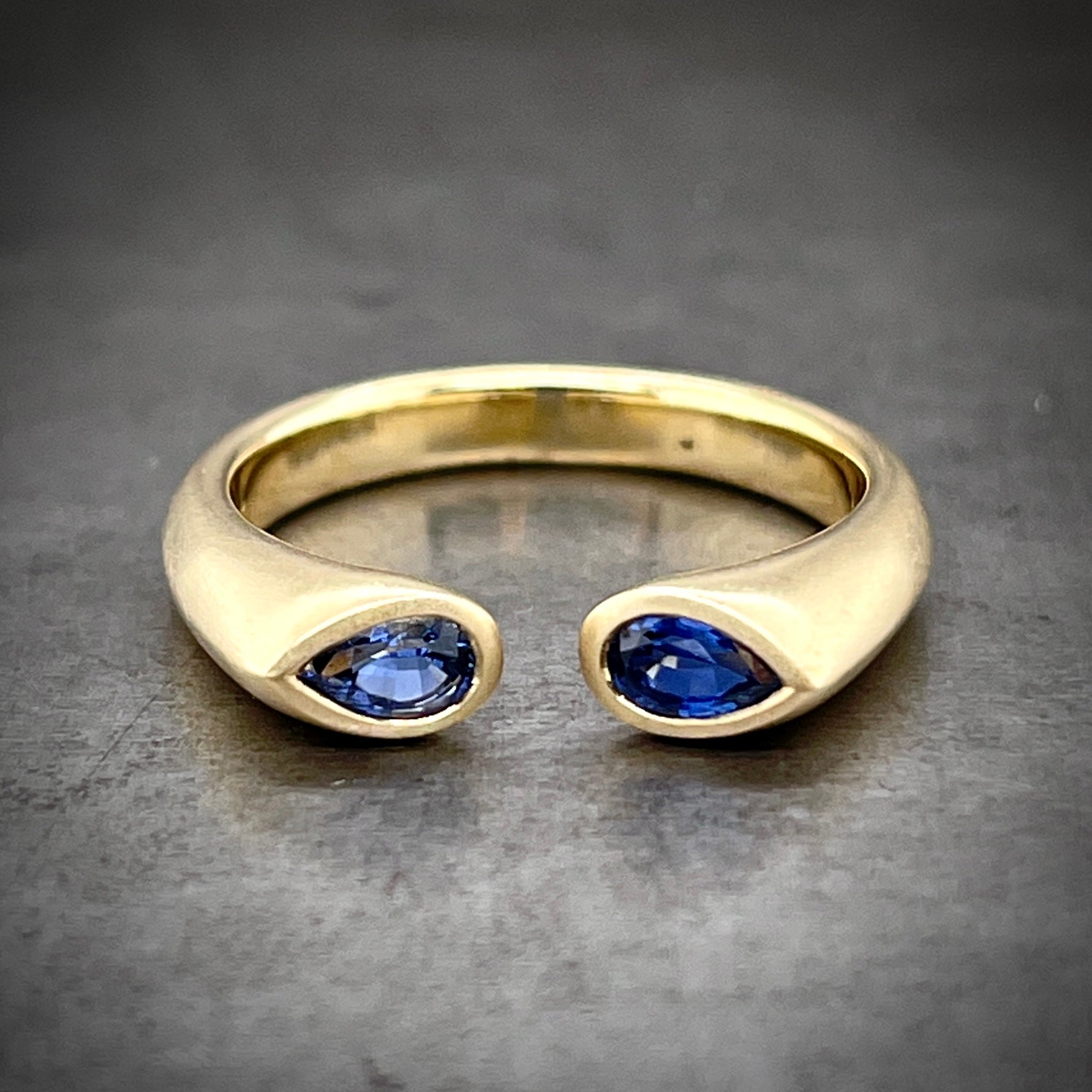 Frontal view of blue sapphire negative space pear cut ring laying down.