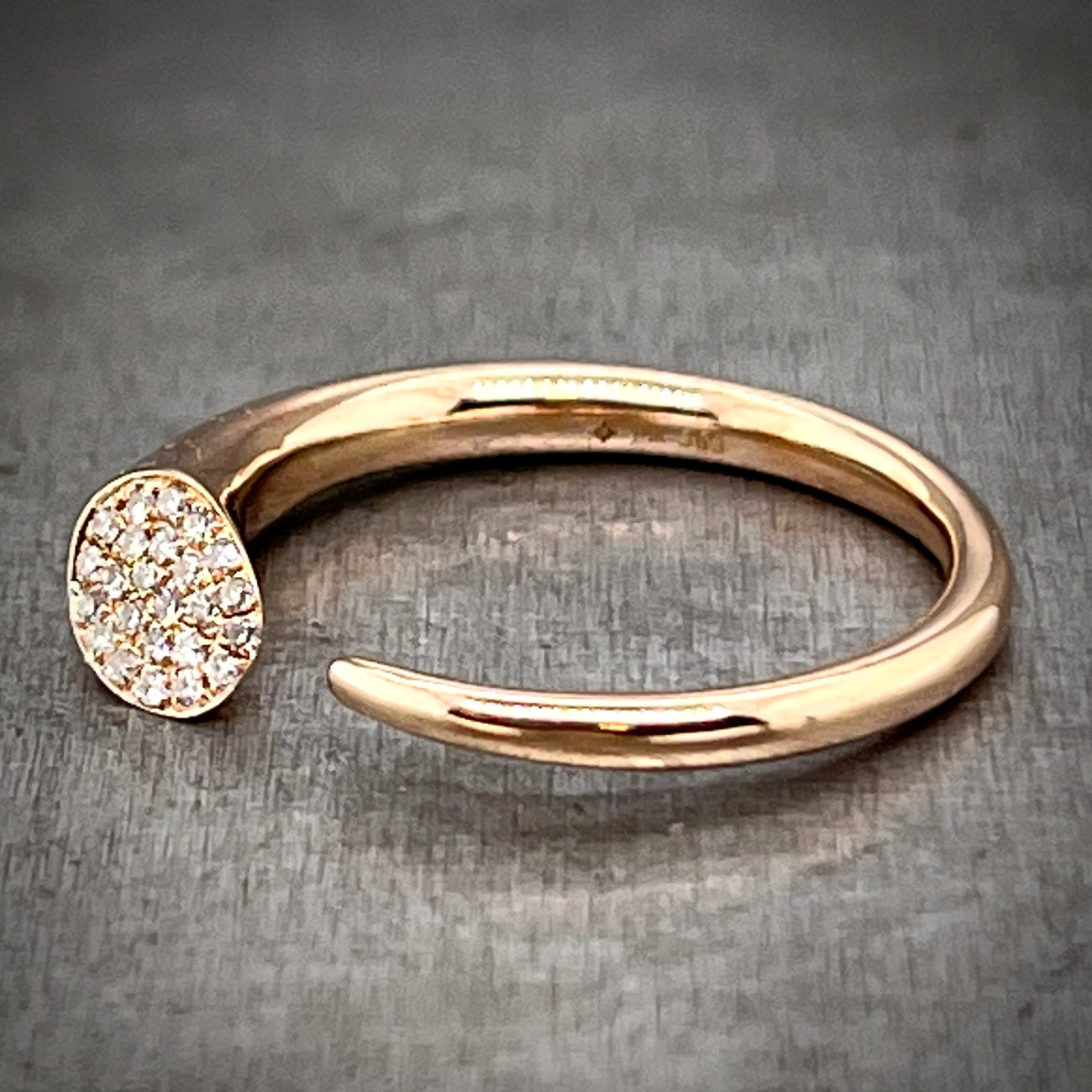Full view of abstract rose gold and diamond ring laying down, angled slightly so you can better see the face of the setting for the diamonds.