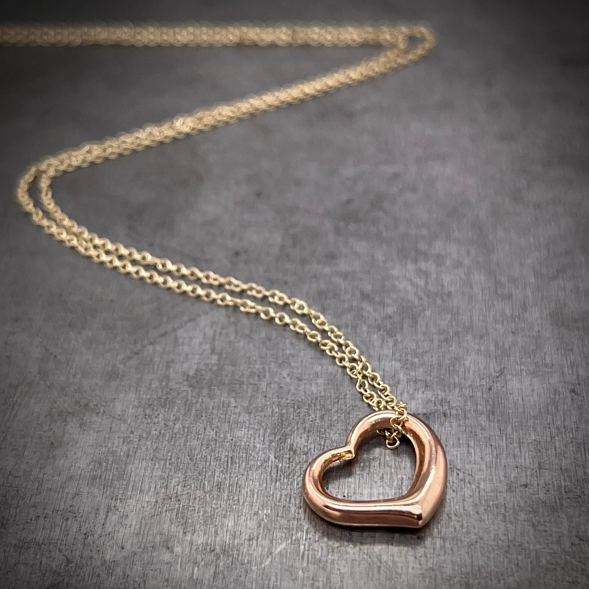 Rose gold heart and yellow chain featured laying down with chain twisting in background.