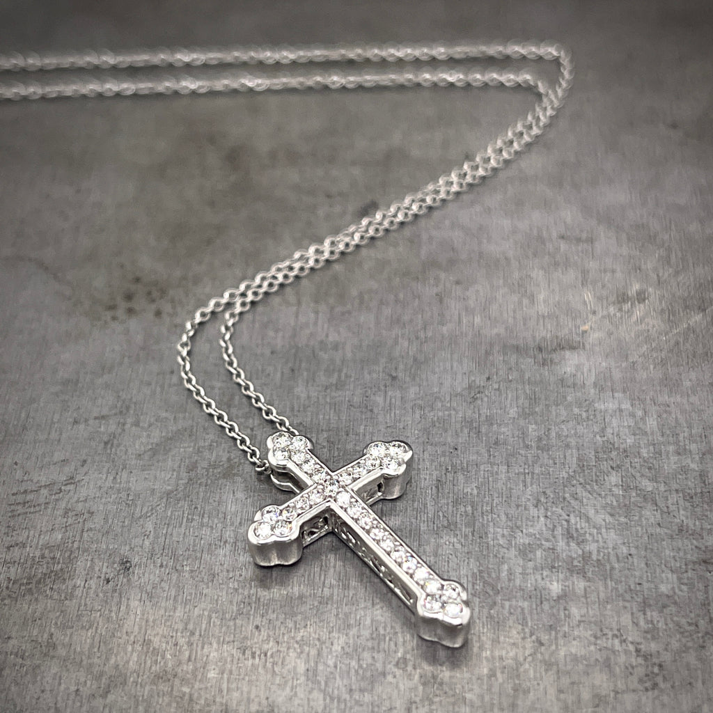 Full view of Diamond Cross necklace laying on gray background with the chain twisting in the background. This cross features one row of diamond on its surface with three diamonds at each point.