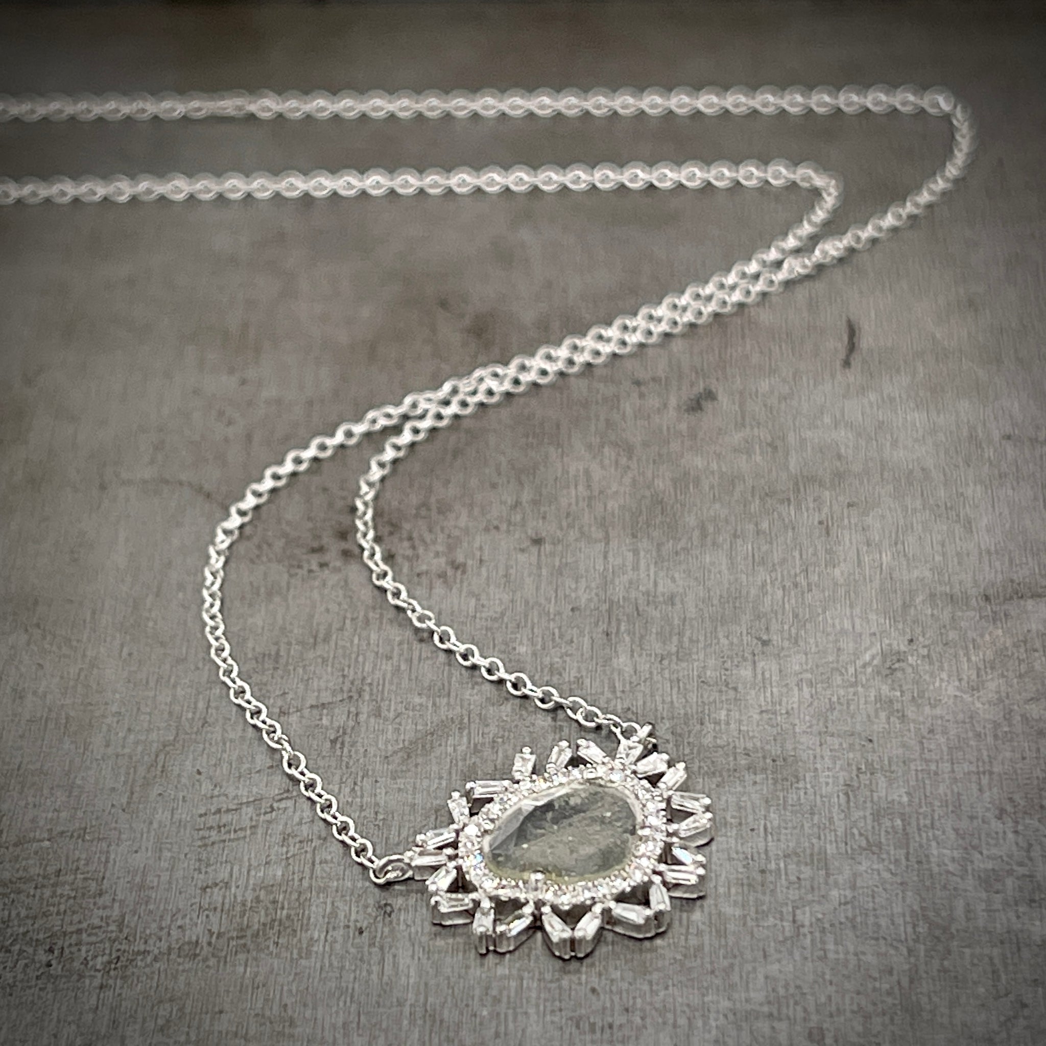 Full view of white gold diamond slice halo necklace laying on a gray background with the chain twisting in the background.