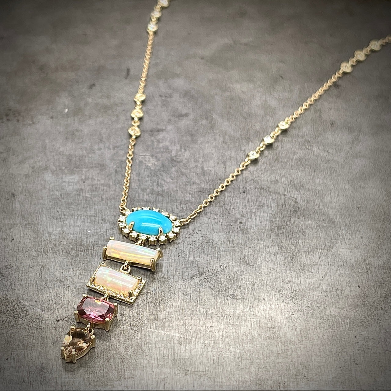 Angled view of 14k yellow gold necklace presents a tapered sequence of colored gemstones, highlighted by diamond accents
