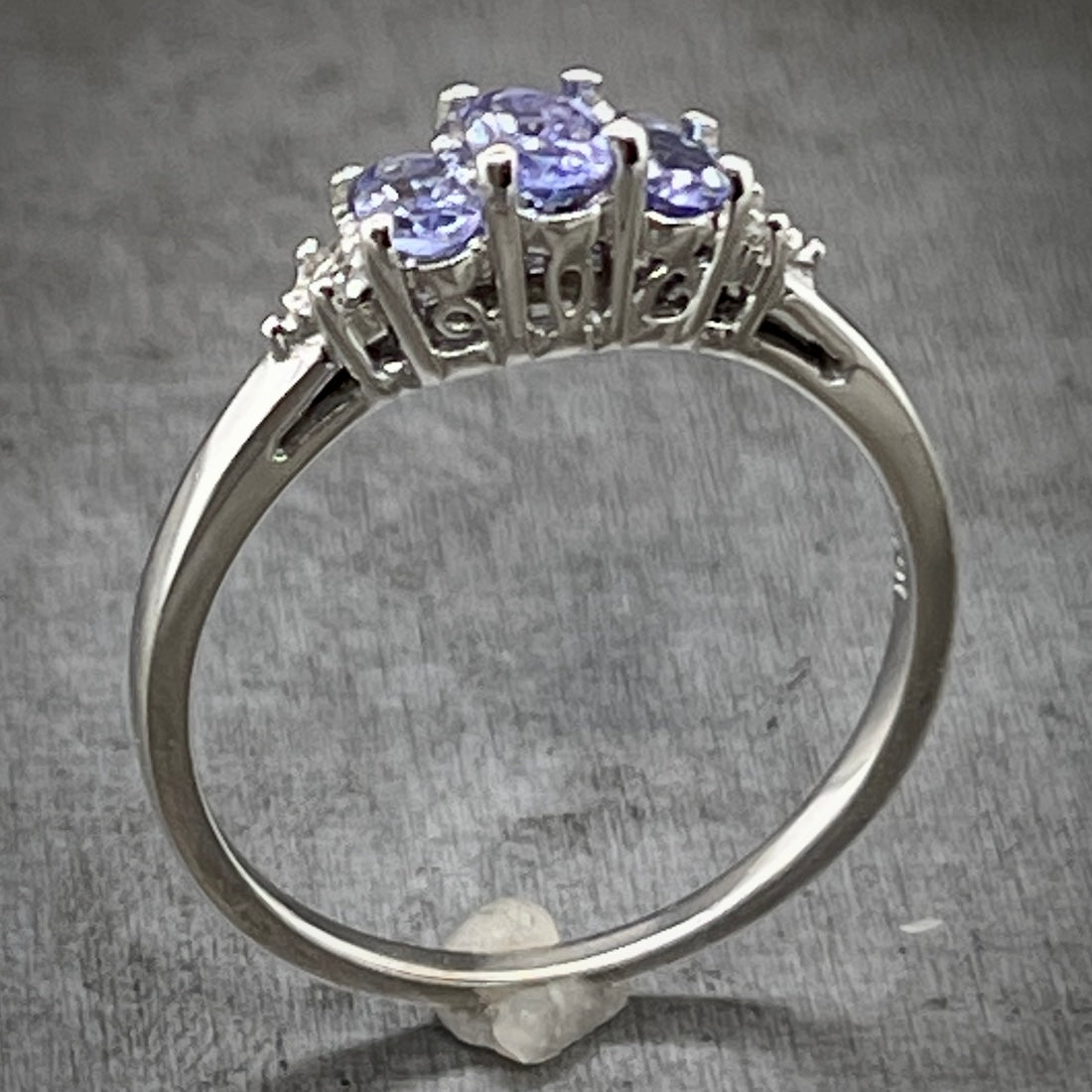 Angled aerial view of white gold tanzanite ring. Here you can better see the head of the ring and its intricate design that showcases a motif of cut out portions of a swirling design.