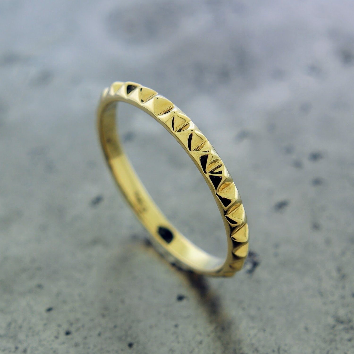 Angled aerial view of 14 karat yellow textured ring. Here you can see the ring features a square pyramid motif. The ring showcases one row of square pyramids that encircle the entirety of the band.