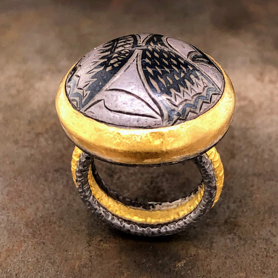 Full view of Turkish button ring. The ring features a gray/black Turkish button on the top that is bezel set in yellow gold. The shank features a hammered gold band with an oxidized silver band on either side of the gold.