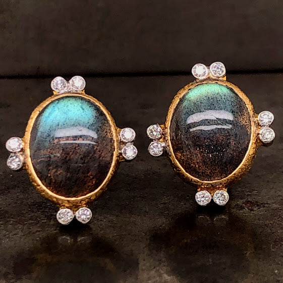 Frontal view of labradorite and diamond stud earrings. These earrings feature one oval cut cabochon labradorite bezel set in yellow gold. Attached to its Northern, Southern, Eastern and Western edges are two round brilliant diamonds that are bezel set and sit right next to each other.