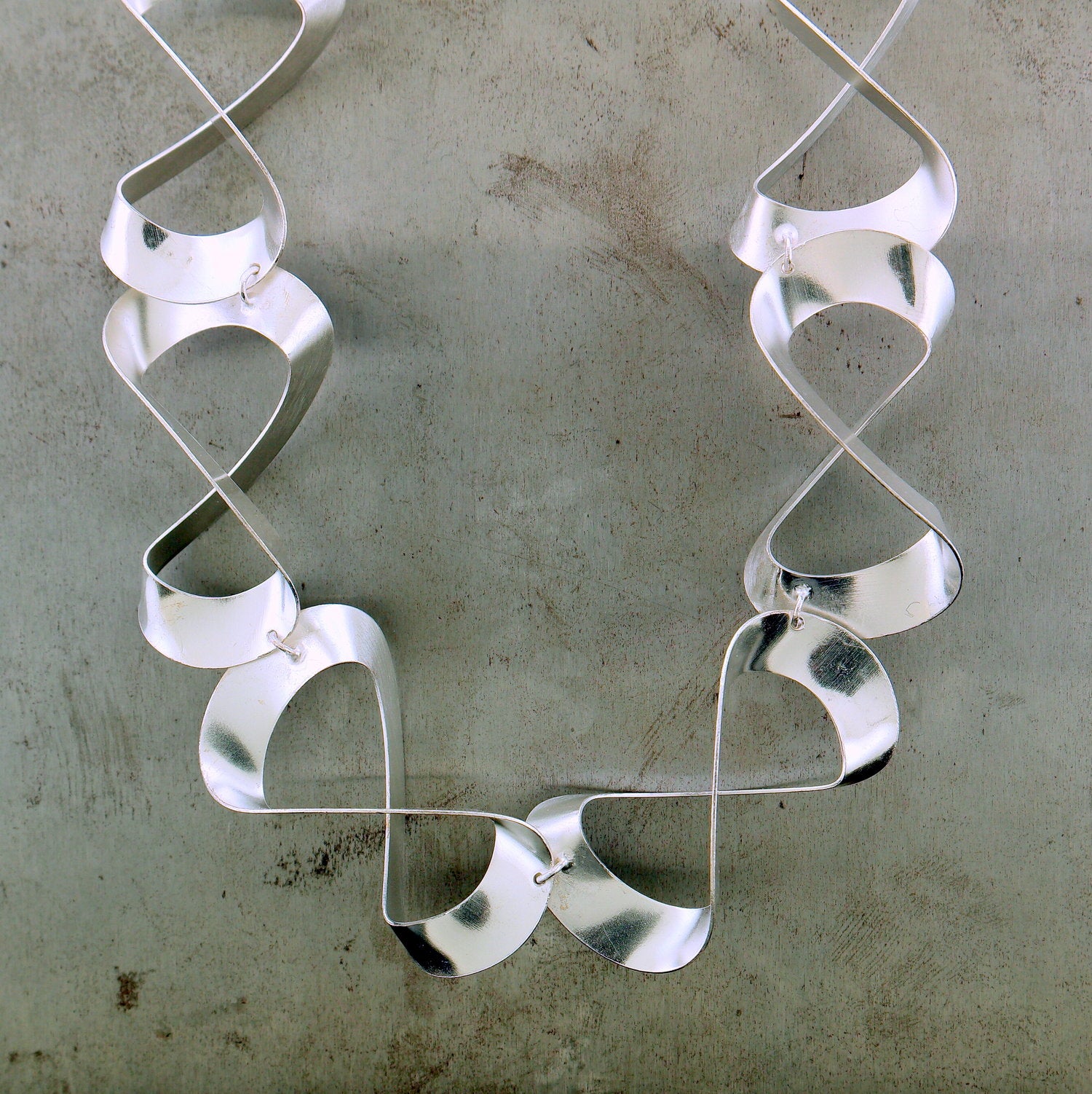 Cropped view of figure 8 necklace. A motif of the figure 8 is created by folding silver. These 8's are connected through a jump ring to one-another.