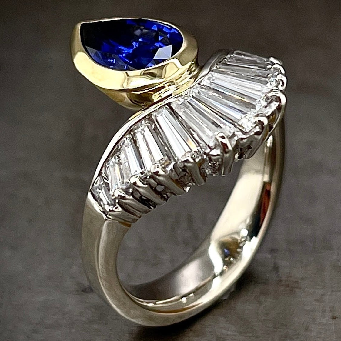 Angled View of Blue Sapphire and Tapered Baguette Ring.  The tapered diamond baguettes face the front of the image.  