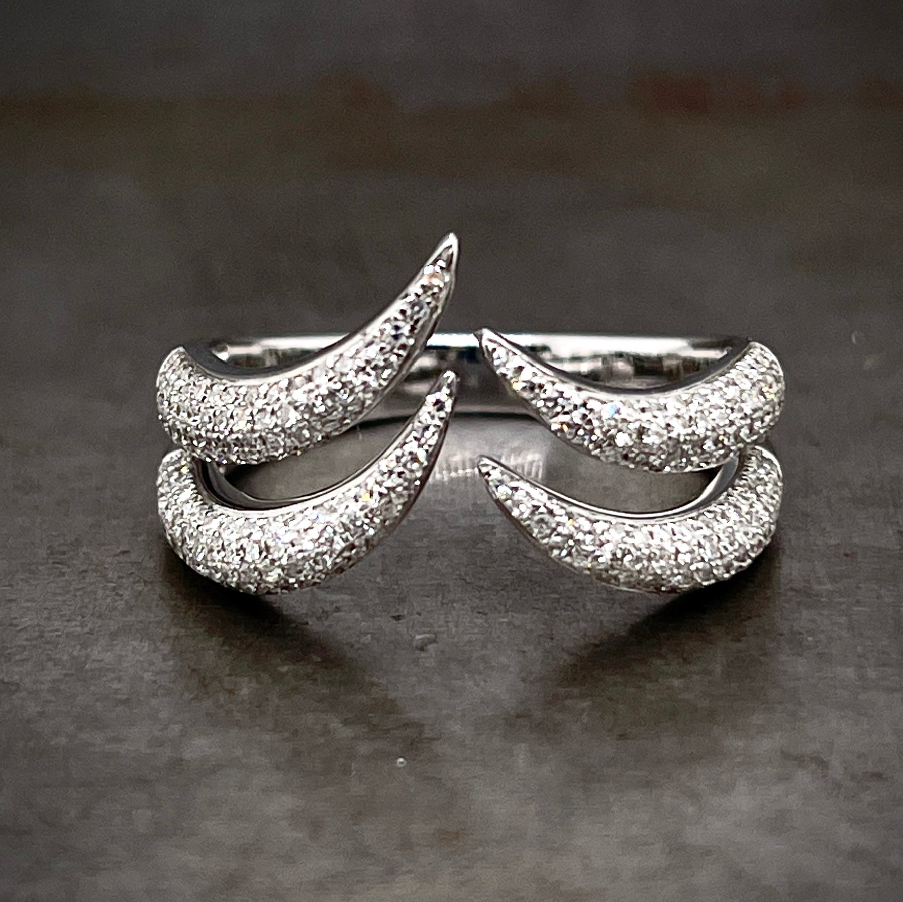 Frontal view of diamond claw ring. Made from 14 karat white gold this ring features two curved claws on the left and right side. The claws curve upward and do not connect, creating a negative space ring. Round brilliant diamonds cover the entirety of the ring.