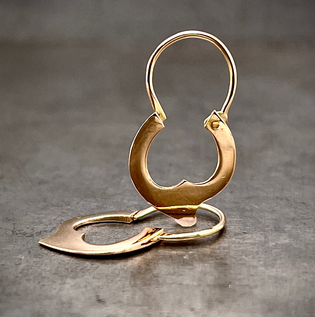 Full view of fire hoop huggie earrings, one laying down and the other standing up. A single flame is carved from gold and created the bottom of the hoops.