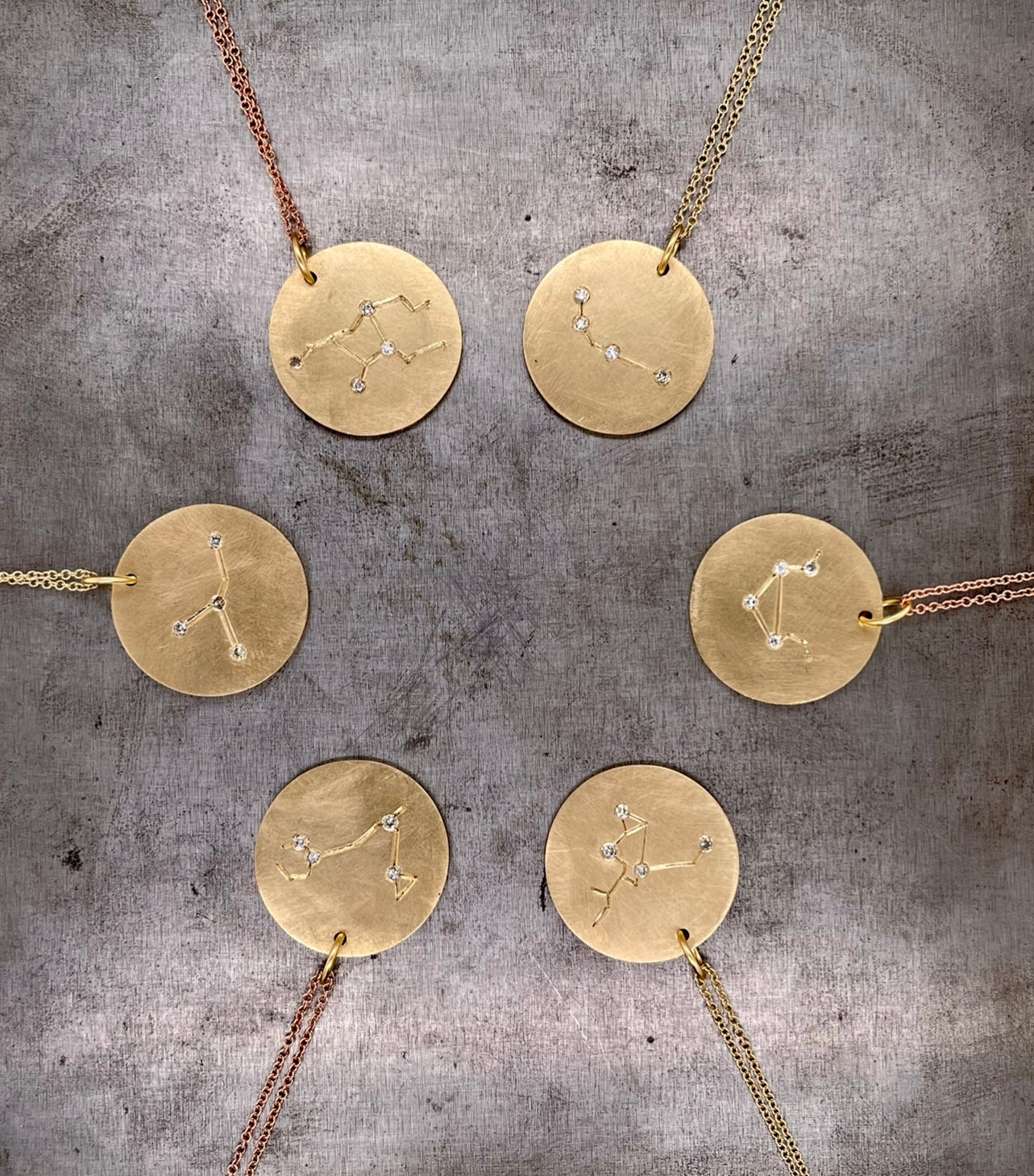Close up view of six zodiac pendants arranged in a circle. The top left features Virgo, and then going clockwise it is Aries, Libra, Sagittarius, Pisces and Cancer.