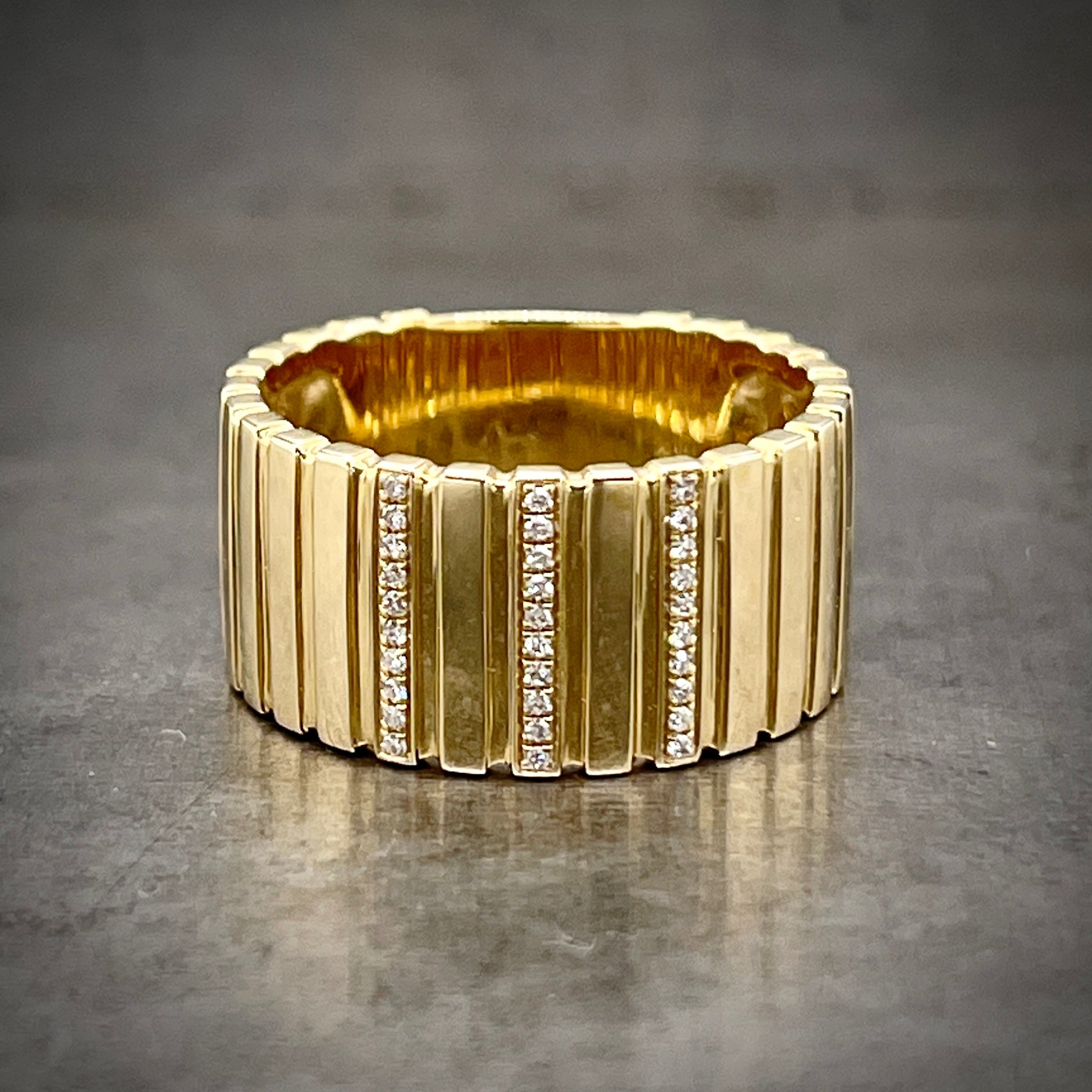 Full view of diamond cigarette band laying down. This band features bars/rectangles of gold through ring. The middle bar features ten round brilliant diamond that cover the entire rectangle. Two rectangles over from either side is another row of diamonds.