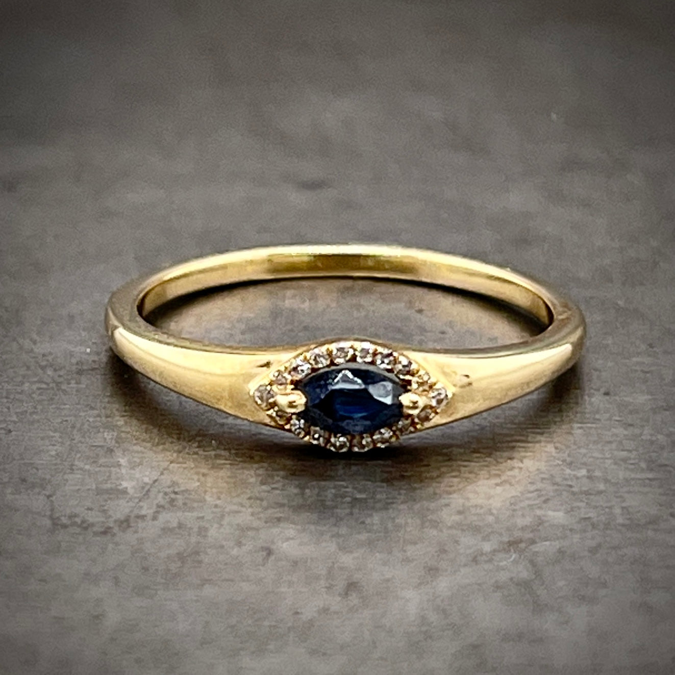 Frontal view of marquise sapphire ring laying down. A marquise cut sapphire (with a rich blue color) is two prong set on the points of the marquise. The marquise is laying western to eastern. A halo of round brilliant diamonds encompasses the sapphire.