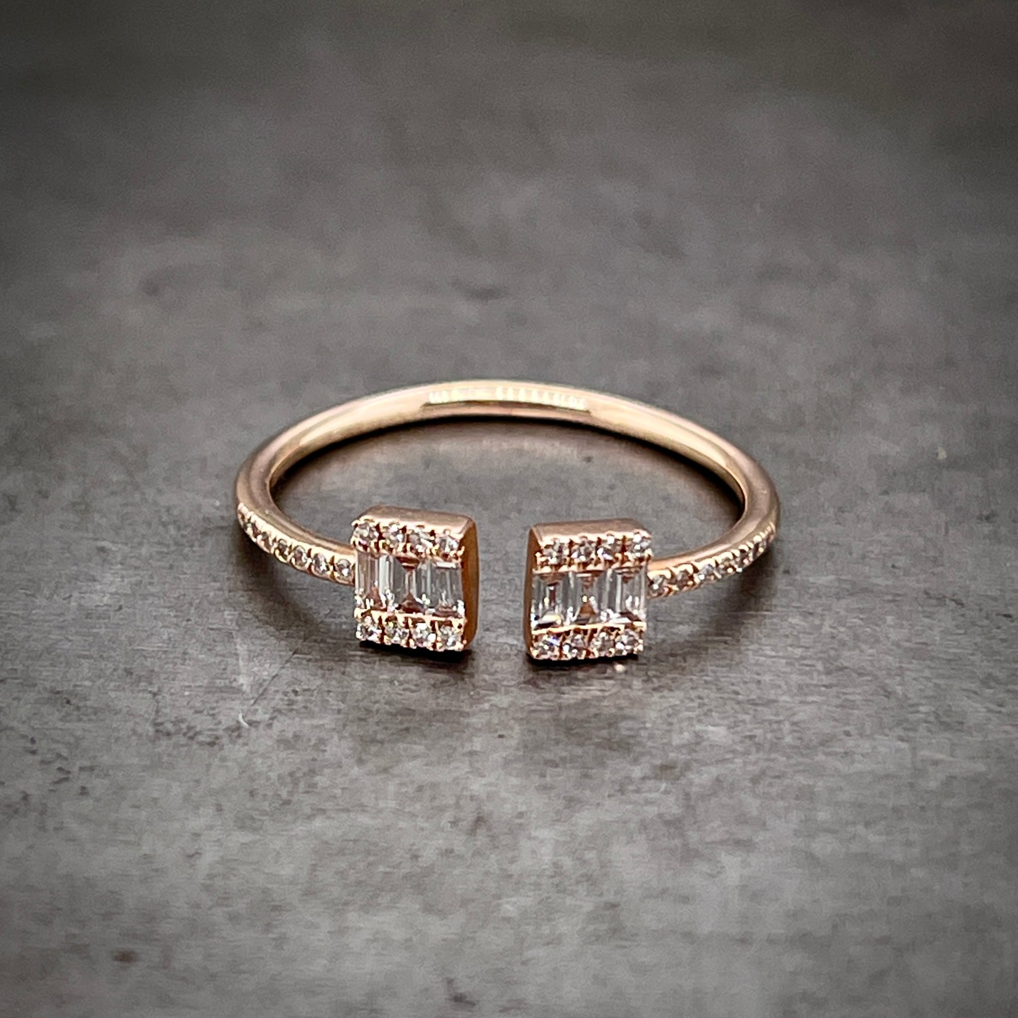 Frontal aerial view of negative space diamond ring. This ring is made from 14 karat rose gold and features round brilliant diamonds on its shoulders. The center of the ring features two rectangle that do not touch one another leaving an open space. The rectangles feature three baguette diamonds in the center and then 4 round diamonds that flank its northern and southern girdles.