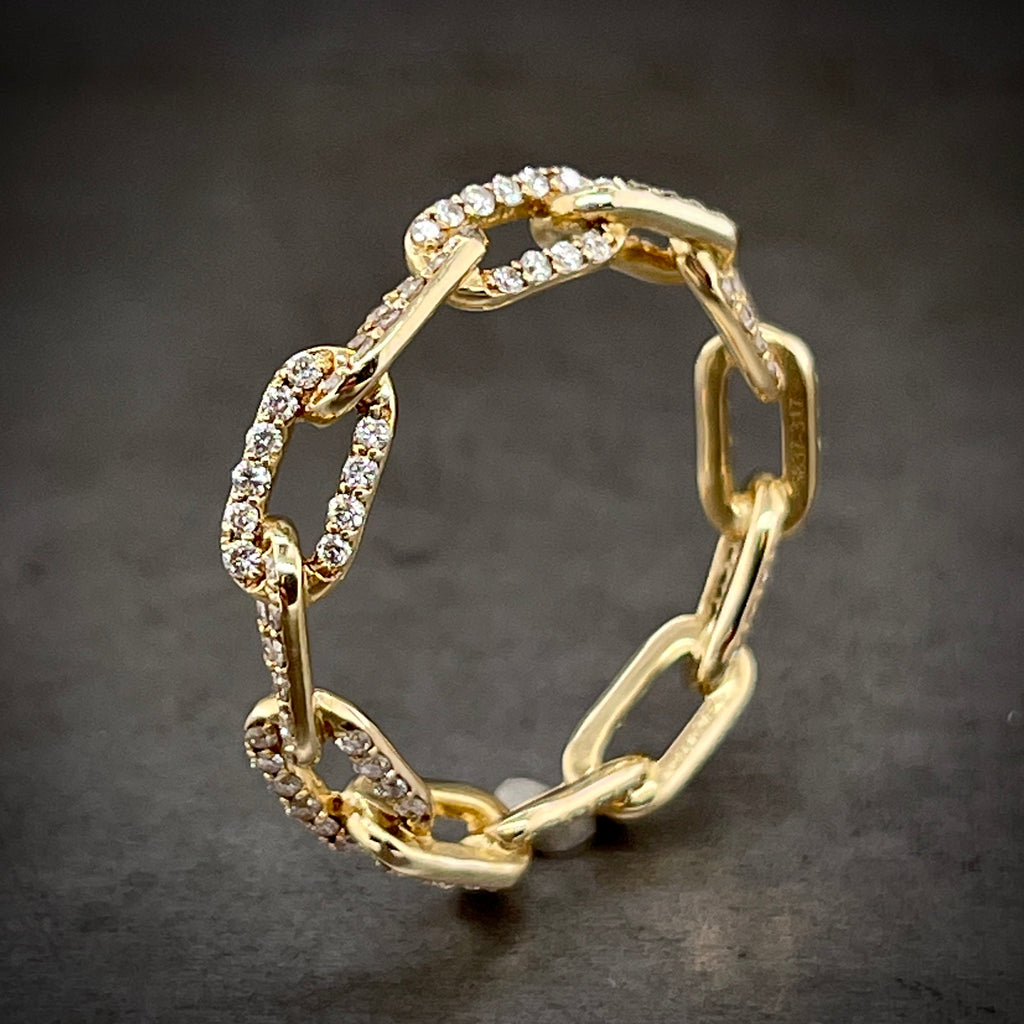 Angled aerial view of diamond yellow gold chain ring. Features curb links that are positioned / angled one to the left, the next to the right, then left, then right, etc.. The top face of each link is covered with a row of round brilliant diamonds.