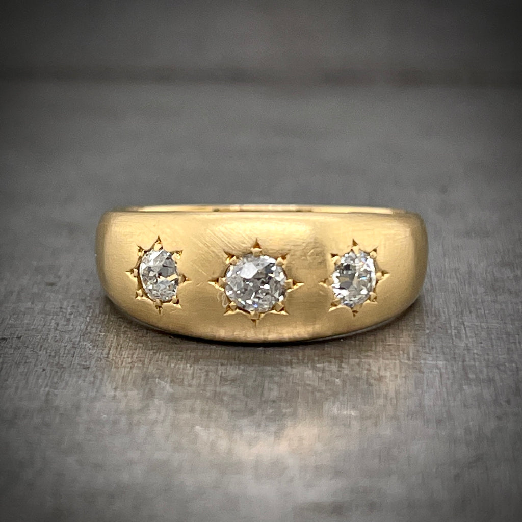 Frontal view of Gold Star Ring. A thicker band of yellow gold that is thickest in the center and slopes down gradually. This ring features three round diamonds set in the center of the band in one row. the setting makes the diamonds look like star with tiny reliefs of triangles in the gold.