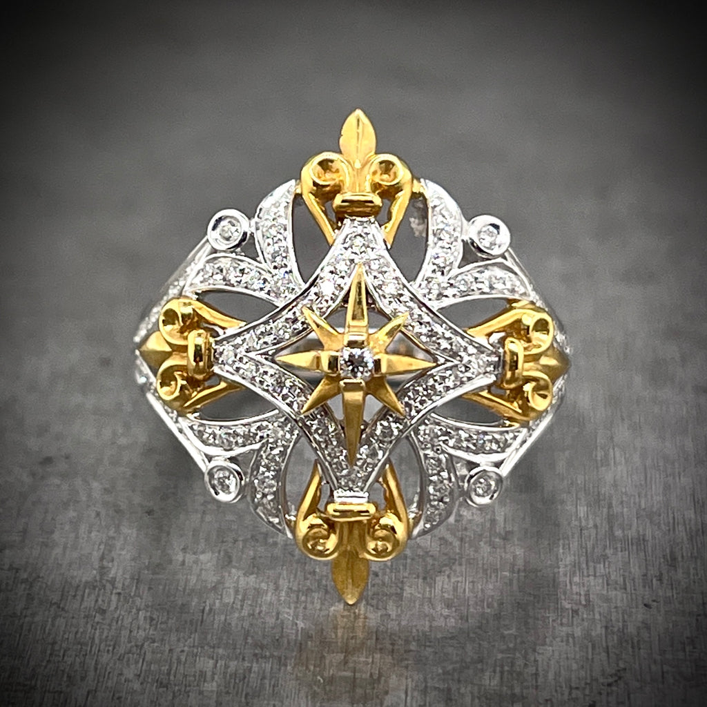 Frontal view of Fleur-de-lis Ring. Made from white and yellow gold, the head features an ornate design with four flour-de-lis at each inter cardinal direction in yellow gold. In the center is a yellow gold star with one diamond. The rest of the ring is white gold with round brilliant diamonds.