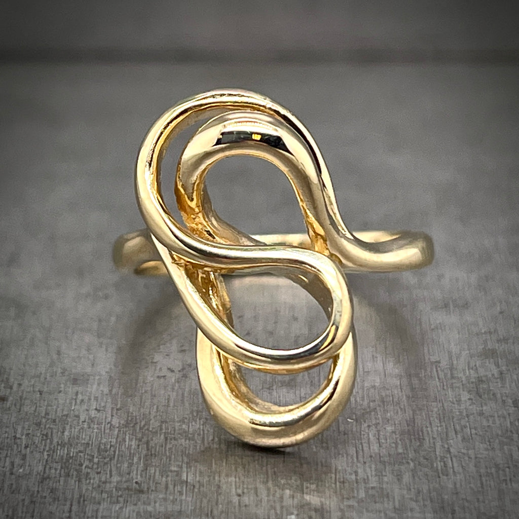 Frontal view of head of Abstract Gold Ring. This ring features line art made from gold wire. The head of this ring resembles two oddly shaped number 8's stacked on top of one another made from gold wire. 