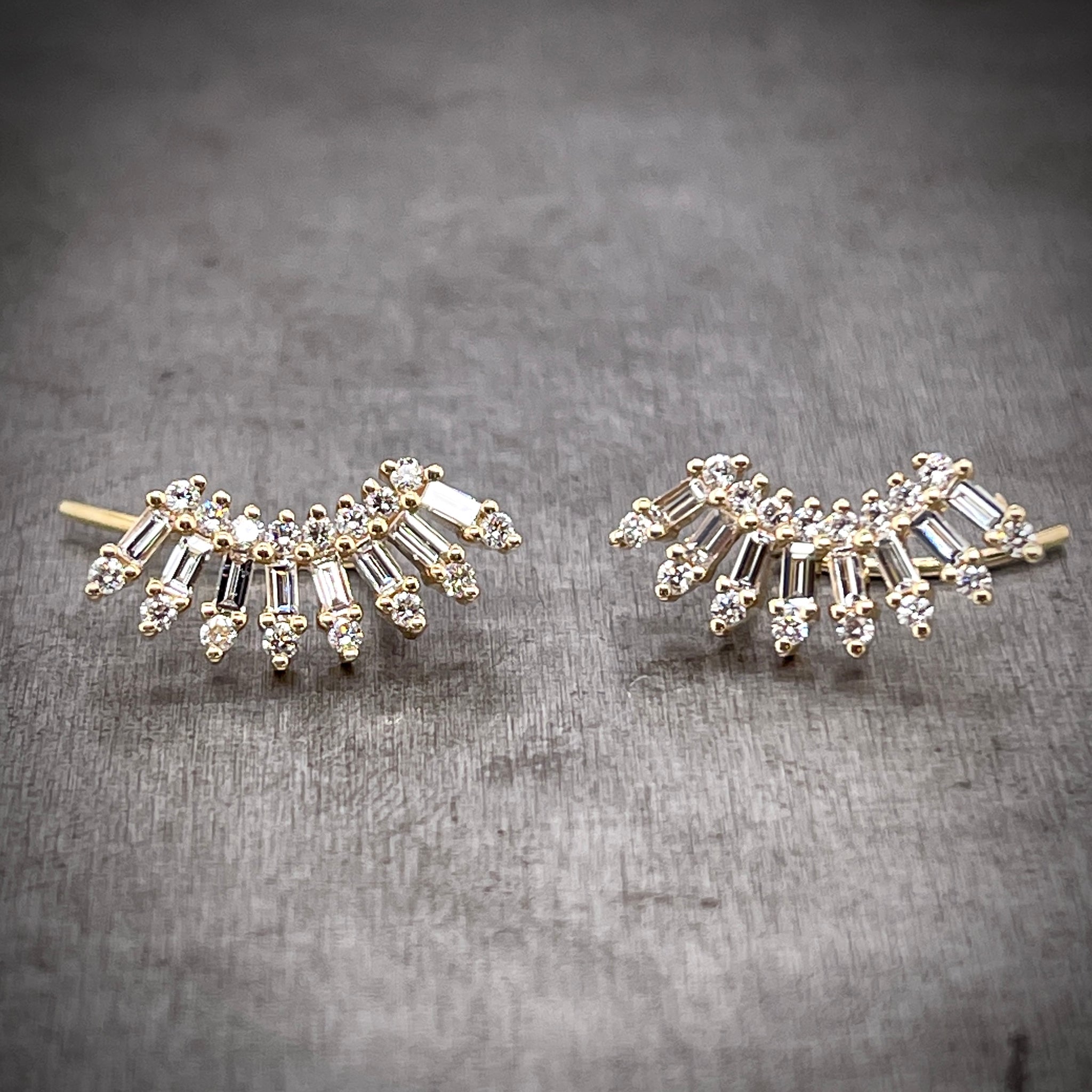 Frontal view of floral diamond ear climbers. These earrings feature a curved silhouette with the first layer being round brilliant diamonds, the second being baguette diamonds and the third being round brilliant diamonds. Each layer fans out more creating the perfect curvature for sitting on your ear.