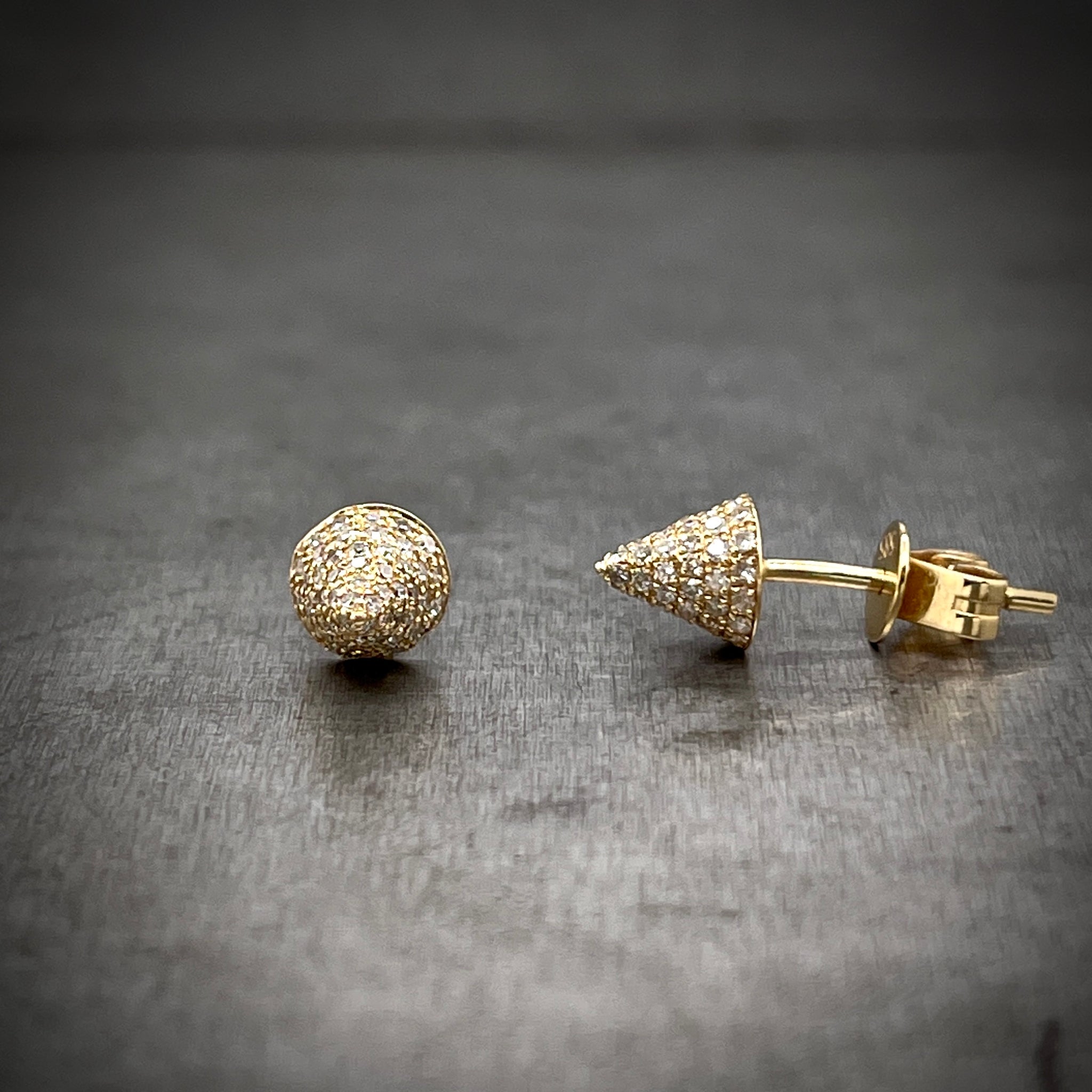 Full view of front and side of Gold and Diamond Spike Studs. The left earring lays straight so the spike is pointed at you and the right earring lays on its side so you can see it post.