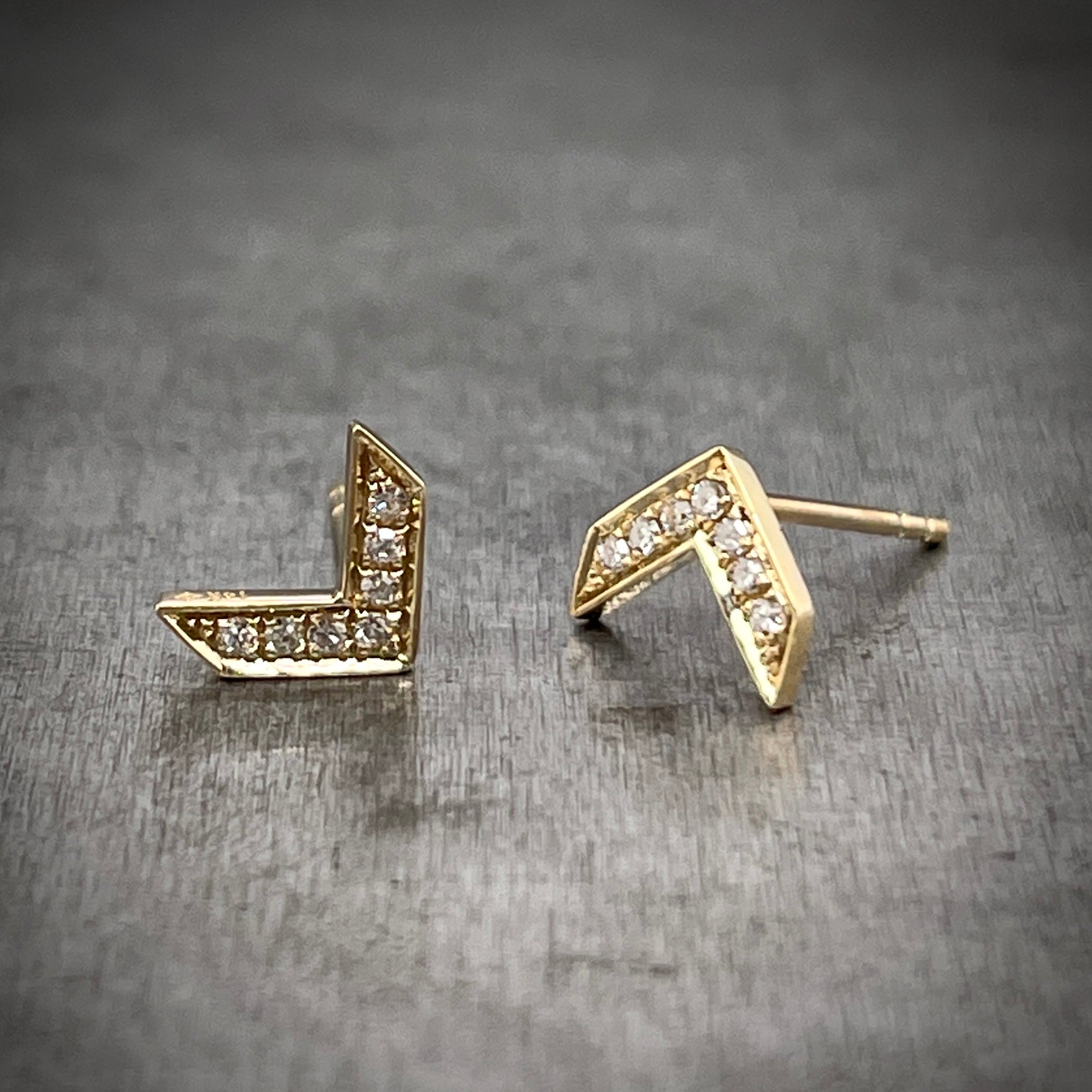 Full and 3/4 profile view of Gold and Diamond Arrow Earrings. The left stud is laying flat and the right is position in an upside-down "V" and angled partially so you can see the post of the stud.