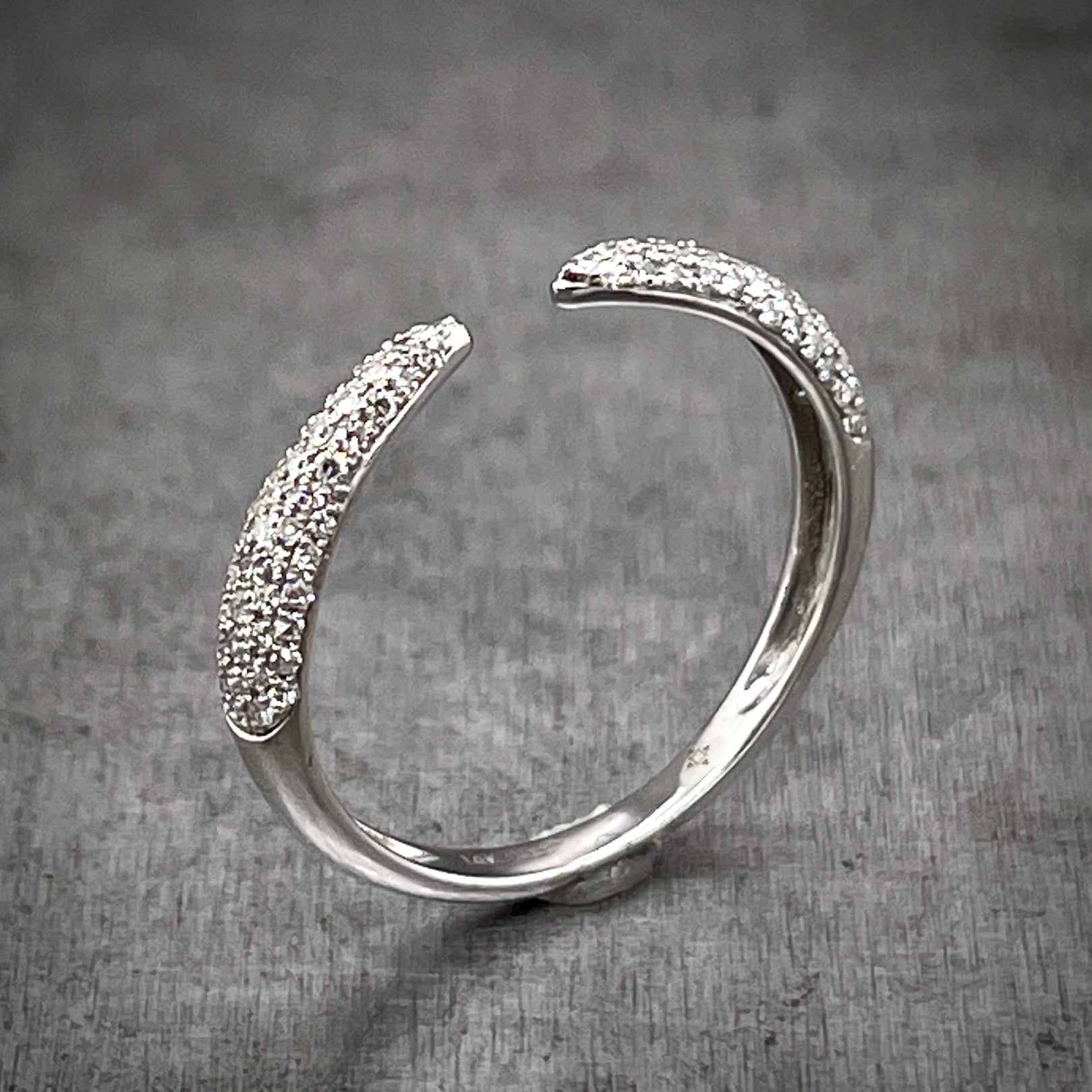 Angled aerial view of single diamond claw ring. Made from 14 karat white gold this ring features what looks like two claws that wrap around a finger and almost touch one-another but stop, leaving a space between them. There are round brilliant diamonds set in the shoulder of the ring.