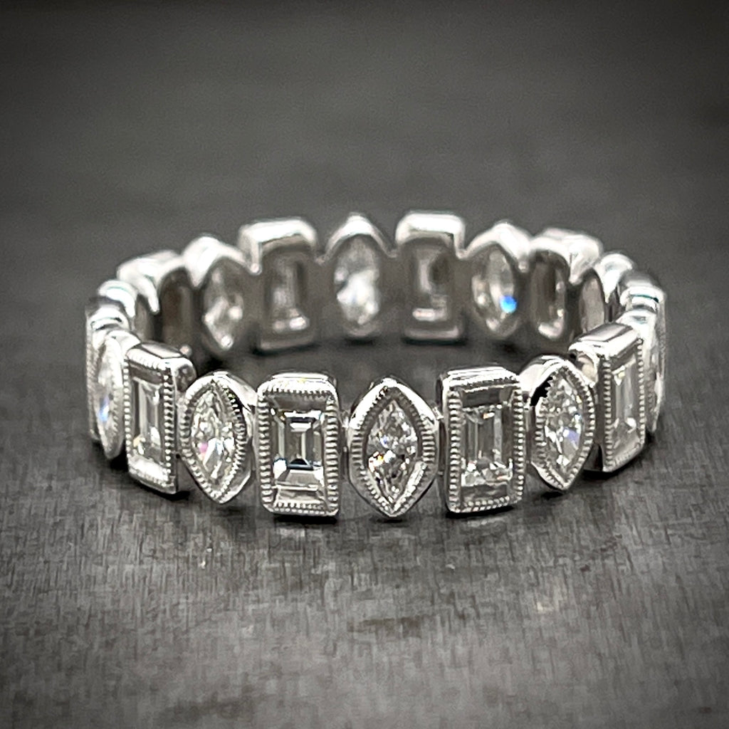 Full view of marquise and baguette diamond eternity band laying down. Ring features marquise and baguette diamonds, facing north to south. The bezels around the diamonds feature migraine detailing.