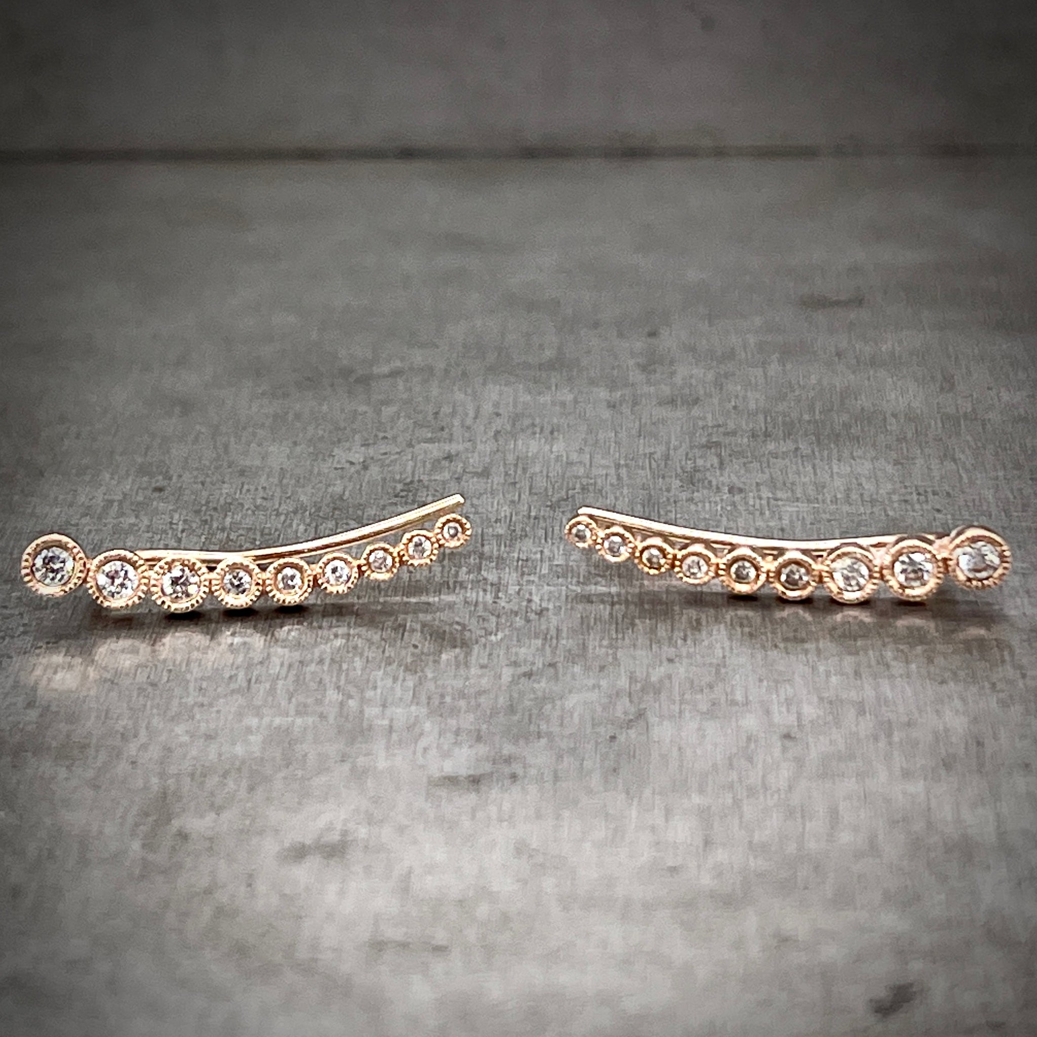 Full view of rose gold and diamond ear climbers laying down. Here you can see the slight curve of the earrings that make the perfect ear slope. The diamonds gradually go down in size, the biggest where the earring starts and the smallest at the end of the slope furthest away from the piercing.