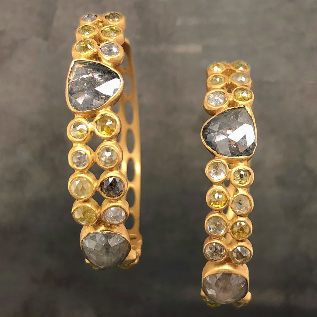 Frontal view of 18 karat yellow gold natural diamond hoops. These hoops feature champagne colored rose cut diamonds. These diamonds are bezel set. There are two rows of round shaped diamonds that go 4 diamonds in length, there there is a triangle like shaped gray diamond that interupts the two rows of diamonds. This pattern continues through the hoops.